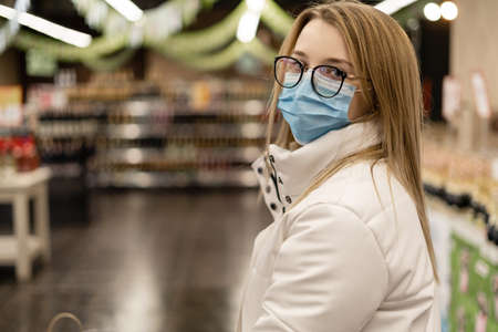 A woman of European appearance in a supermarket buys goods. Face mask and virus protection in public places. Covid19 flu in a crowded place.の写真素材