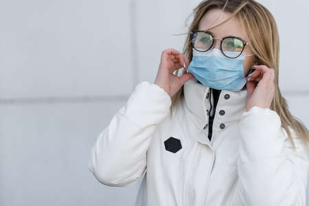 Beautiful young european woman in clothes outdoors with a medical mask on her face. Close up portrait of a woman in a respirator to protect against infection with influenza or coronavirusの写真素材