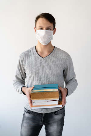 training during quarantine, a young guy holding books in his hands wearing a protective mask. Place for textの写真素材