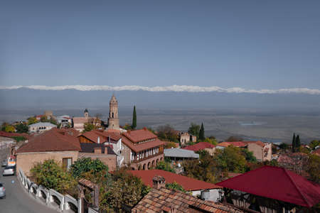 The landscape of the city of Sighnaghi near the mountains of the Caucasus in Georgia, a church with a bell tower, buildings and roofs, as well as mountain ranges. top view place for text sunny day with blue sky and white cloudsの写真素材