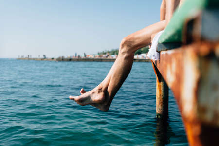 a man sits on a pier legs lowered into the water. Rest in the summer at the resort. Place for textの写真素材