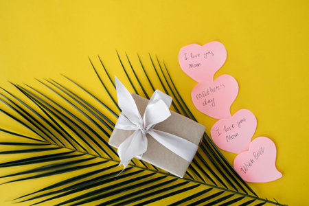 on a yellow background lies a box with a gift, a pink bow, a green palm branch. Sticky leaves with...