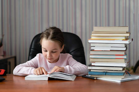 A curious little girl, a child with pleasure, reads a book and takes lessons. Quarantine home training concept.の写真素材