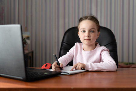 online education concept online. A little girl sits at home, looks into a laptop and writes an abstract. Online school concept.の写真素材