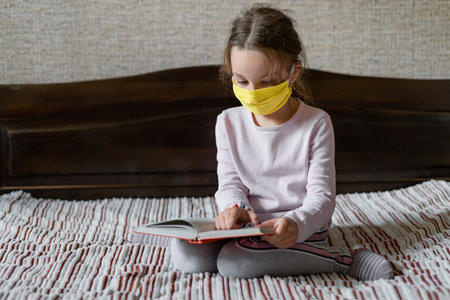 little girl schoolgirl is engaged in school remotely. The concept of distance education during a pandemic and quarantine. Medical mask is put on faceの写真素材