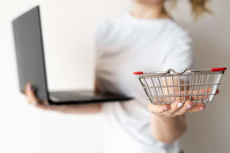 online shopping concept, woman holds shopping basket in one hand. A laptop in the other hand. Place for textの写真素材