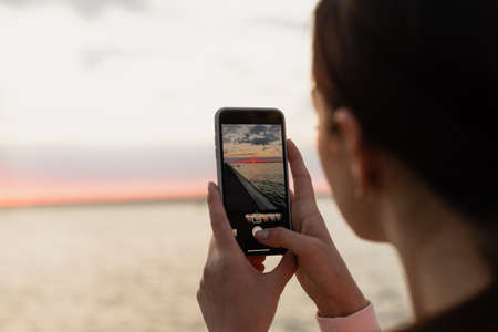 A young girl, an athlete, after a bike ride, came to the sea, photographs the dawn, looks at the sea and rests from doing sports.の写真素材
