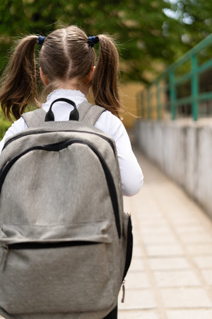 The young student returns to school. Morning walk with a backpack. Head down, the child goes for...