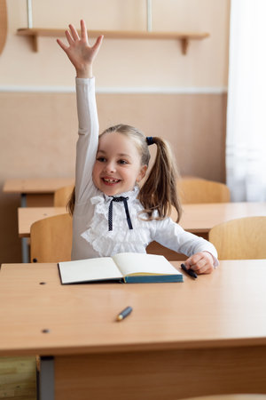 girl schoolgirl sits at a lesson at her desk. He pulls his hand very strongly up. He knows the...