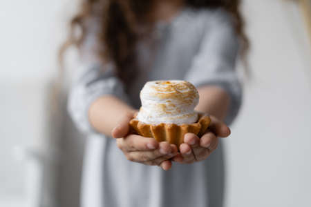 Holiday. A girl with wavy hair is standing against the wall. Birthday. In the hands of a child a cake with white cream and a basket of shortcrust pastry. Arms extended forward.の写真素材