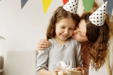 Birthday concept. A young woman and her beautiful daughter are smiling and laughing. Mother kisses her child. Happy mom gave a gift and the baby is happy. White background. 7 years. Family traditions.の写真素材