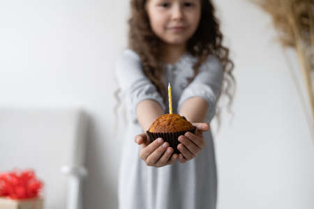 Lovely girl holding in hands cupcake with one candle, body part, happy holiday celebration, birthday partyの写真素材