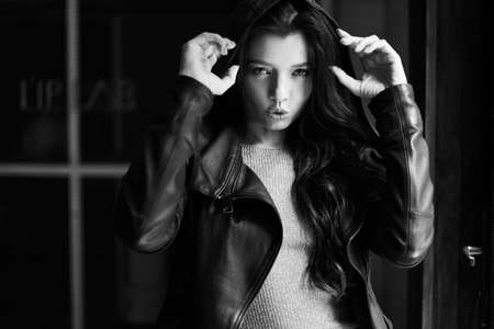 Gorgeous brunette girl with curly hair. Black and white photo. The lady is wearing a leather jacket. Her look is aggressive and seductive.の写真素材