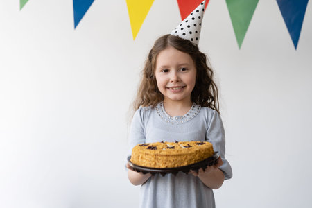 Happy cheerful girl with curly flowing hair holds a cake in her hands. It's her birthday. She stands...