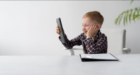 A schoolboy is doing quarantine homework at home. Distance learning child. The boy is sitting in...