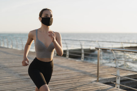 beautiful woman runs early in the morning along the promenade. A medical mask is worn on the face....