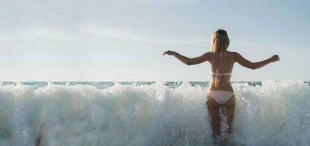 Sexy young girl during a hot summer day jumps in the sea waves. Back view. Travel, active, yoga, lifestyle freedom concept. Vacation on the ocean. Place for text. Copy spaceの写真素材
