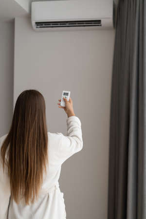 a young woman in a hotel holds a remote control from the air conditioner in her hands. Regulates the temperature in the room. Place for textの写真素材