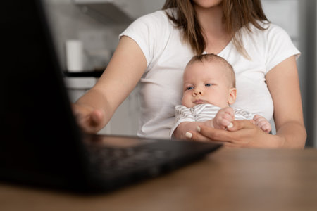 Close up portrait of a nursing baby. The boy sits in his mother's arms. A woman works at home with a...