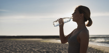 beautiful young woman drinks water after a workout. Exercise at sunset in the evening. Ocean. Place...