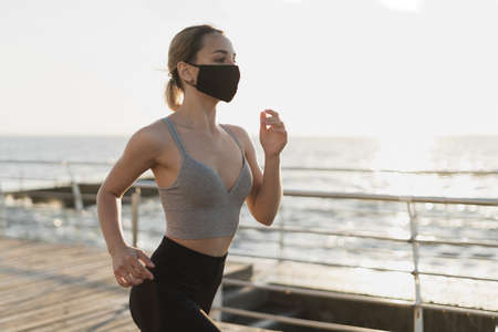 close up portrait. woman runs early in the morning along the promenade. A medical mask is worn on the face. Virus protection during an epidemic.の写真素材