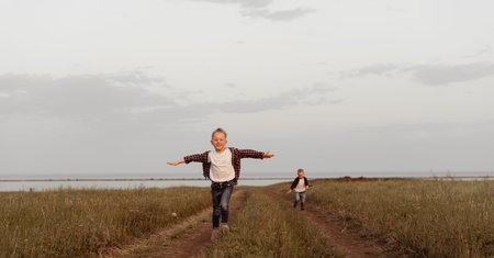 A little boy in jeans clothes runs, arms outstretched towards the viewer across the field. The sky is cloudy. Image with a selective focusの写真素材