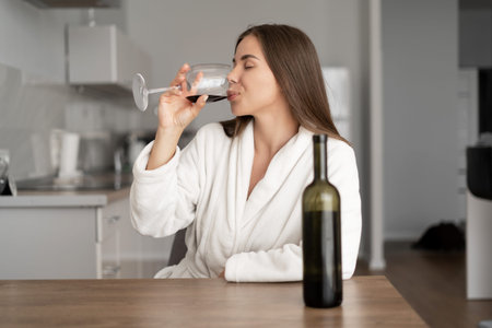 young beautiful woman is sitting in the kitchen. to drink wine in the evening after work. Drink...