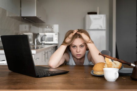 Depressed upset young woman is pulling her hair while using a laptop at home for remote job in her...