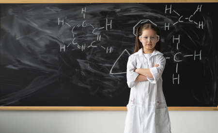 serious young girl science student with glasses in lab coat with hand drawings science formula, back to school and successful female career concept. Space for text, copy space.の写真素材