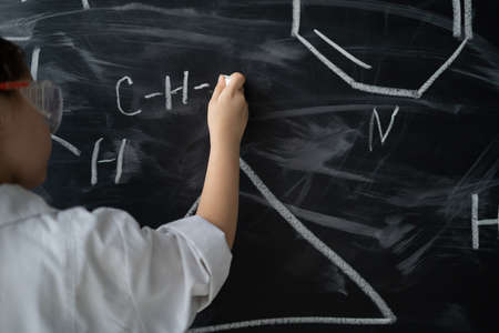 close-up of a girl's hand. Hold white chalk and write formulas in chemistry lesson. blackboard. Back to school concept. Offline educationの写真素材