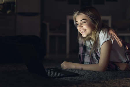 young beautiful woman at night watching a movie on a laptop. Cinema online. A fun comedy before bedの写真素材