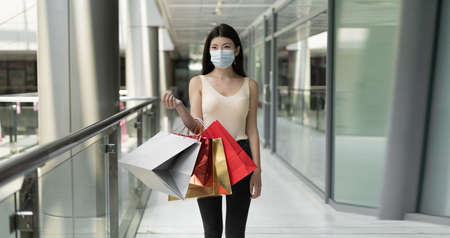 Young beautiful Korean woman stands in a shopping mall. Holds shopping bags in his hands. Protective medical mask worn on the face.Place for textの写真素材