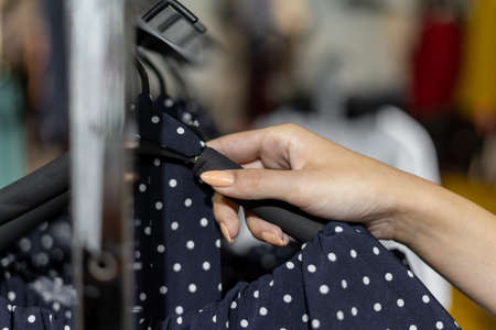 Close-up of a woman's hand takes off a dress from a hanger. Women's clothing shopping concept.の写真素材