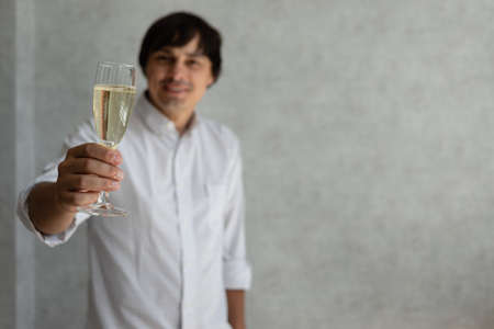 A young guy raises a glass of champagne in honor of the holiday. Place for text.の写真素材