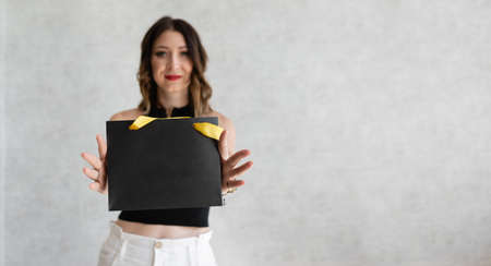 Young beautiful woman on a gray background holds a black gift bag in her hands. Space for text copy spaceの写真素材