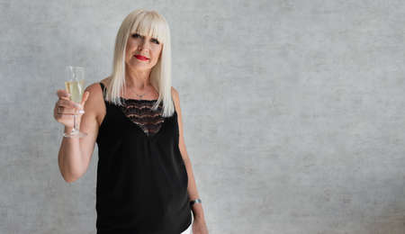 An adult woman on a gray background with a glass of champagne celebrates Christmas and New Year. Aged blonde. Place for text. Copy spaceの写真素材