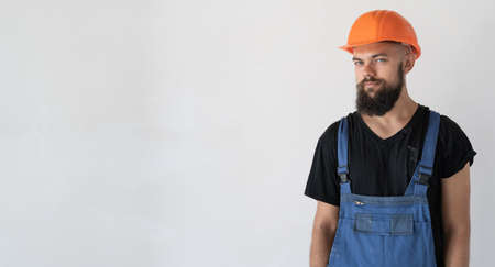 a man builder is dressed in special clothes and an orange hard hat stands near a white wall. Copy spaceの写真素材