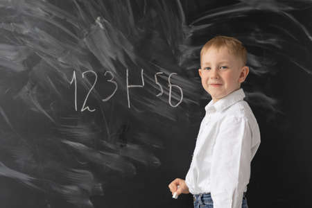 audience at school, offline education. A little boy of 6 years old is standing near the blackboard. Write numbers in chalk. Error completing taskの写真素材
