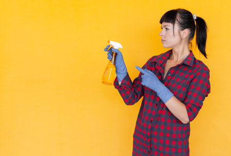 Female hand in blue protective glove holding yellow spray bottle, hand point finger to copy space....