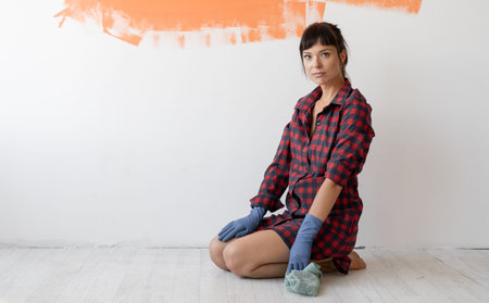 young tired woman in a red shirt sits on the floor. hand wash the floor with a microfiber cloth and...