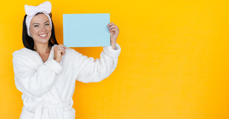 a woman in a white bathrobe and a bandage on her head holds a blank sheet of paper in her hands....