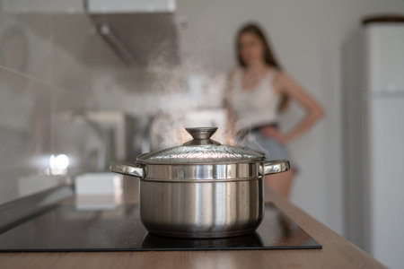 Close-up of a saucepan with boiling water on the stove. A young woman stands aside. The concept of...