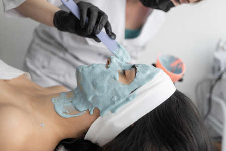 Beautiful young woman at the reception at the beautician, alginate mask, the process of applying to the face, side view. Close-up. Cosmetic procedure in a modern beauty salon. personal hygiene. Place for textの写真素材