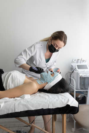 Beautiful young woman at the reception at the beautician, alginate mask, the master apply on the face side view. Close-up. Cosmetic procedure in a modern beauty salon. personal hygiene. Place for textの写真素材