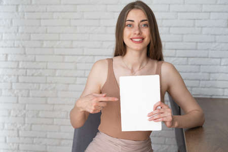 young beautiful woman vlogs video at home. He holds a blank sheet of paper in his hands and points at it with his finger. Empty space for textの写真素材
