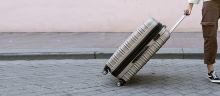 gray suitcase on wheels on the sidewalk. Luggage stands on the street of the city and is ready to...