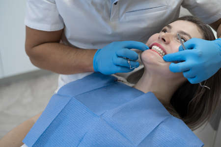 male dentist bent over a woman looks at her jaw. Show the bite to the doctor.の写真素材