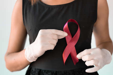 healthcare and medicine concept - female hands in medical gloves holding red AIDS awareness ribbon.の写真素材