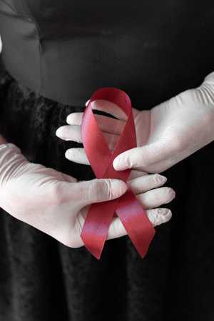healthcare and medicine concept - female hands in medical gloves holding red AIDS awareness ribbon.