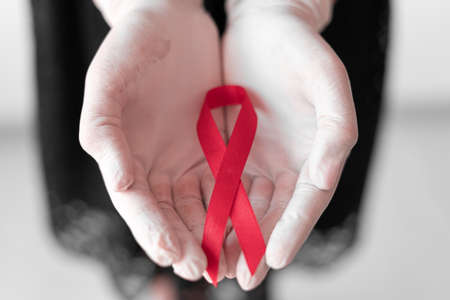 healthcare and medicine concept - female hands in medical gloves holding red AIDS awareness ribbon.の写真素材
